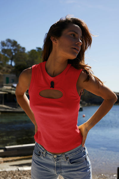 Woman wearing a red sleeveless top with cut-out design by a body of water.