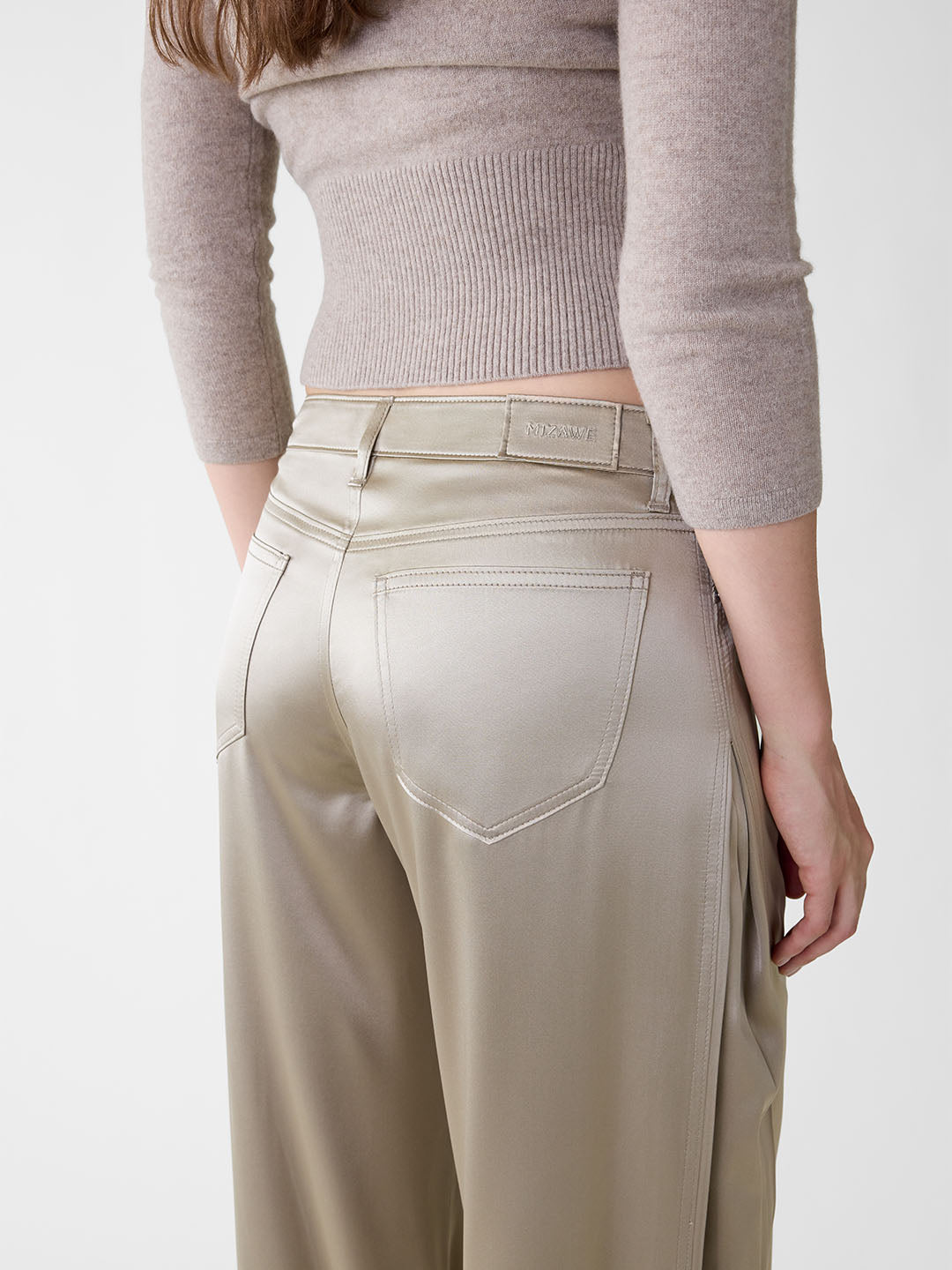 Khaki stretch silk wide-leg jeans with five-pocket styling, mid-rise waist, and side pleats on a model.