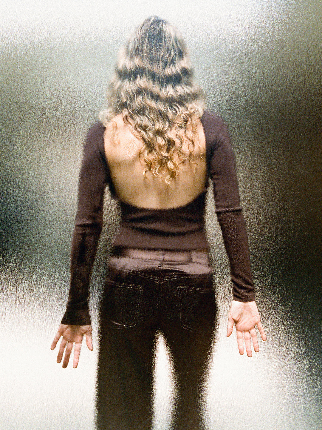 Woman wearing a chocolate brown, lightweight cashmere sweater with a sculpted open back and long sleeves.